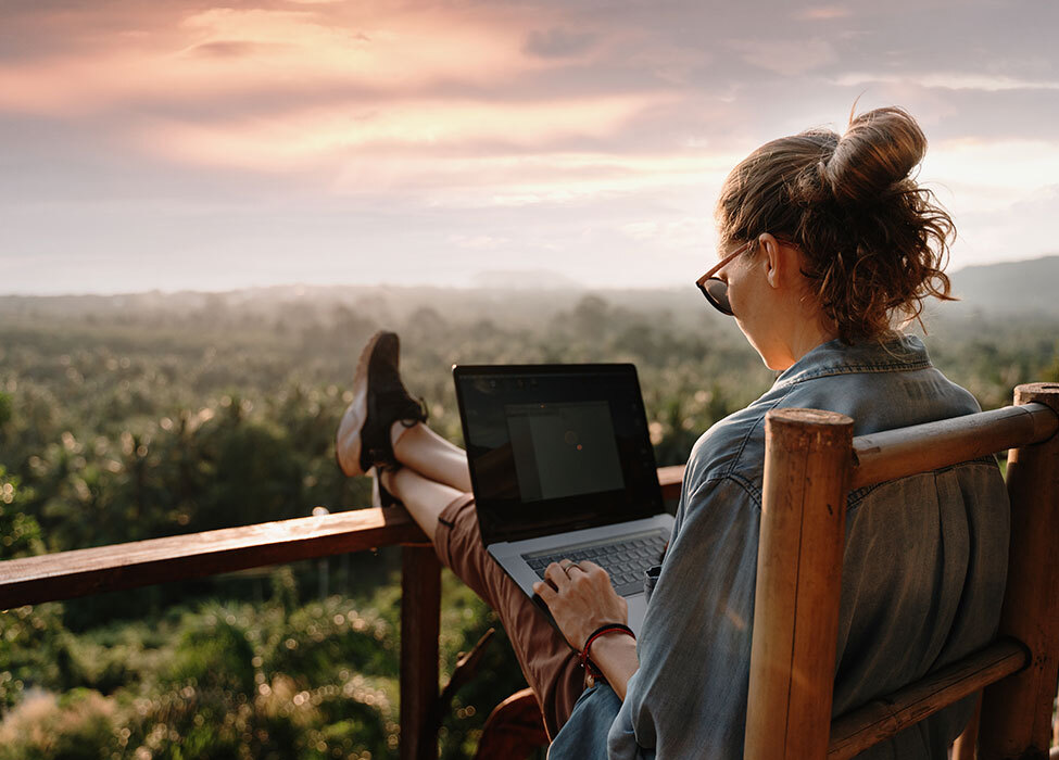 work-life balance and work-life freedom | person sits on balcony with their feet propped up on railing while working on their laptop