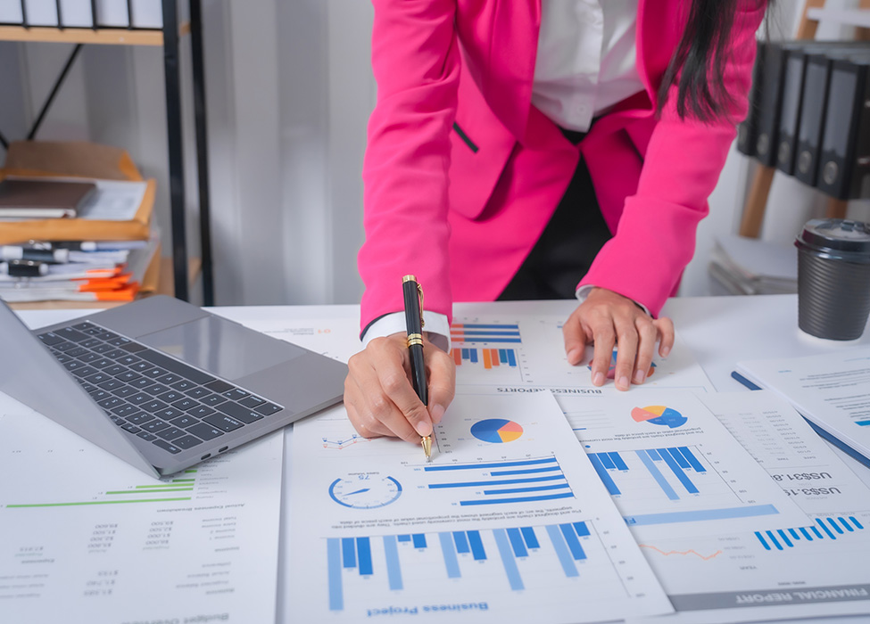 Graphs spread out on a table with a person leaning over and making notes on them