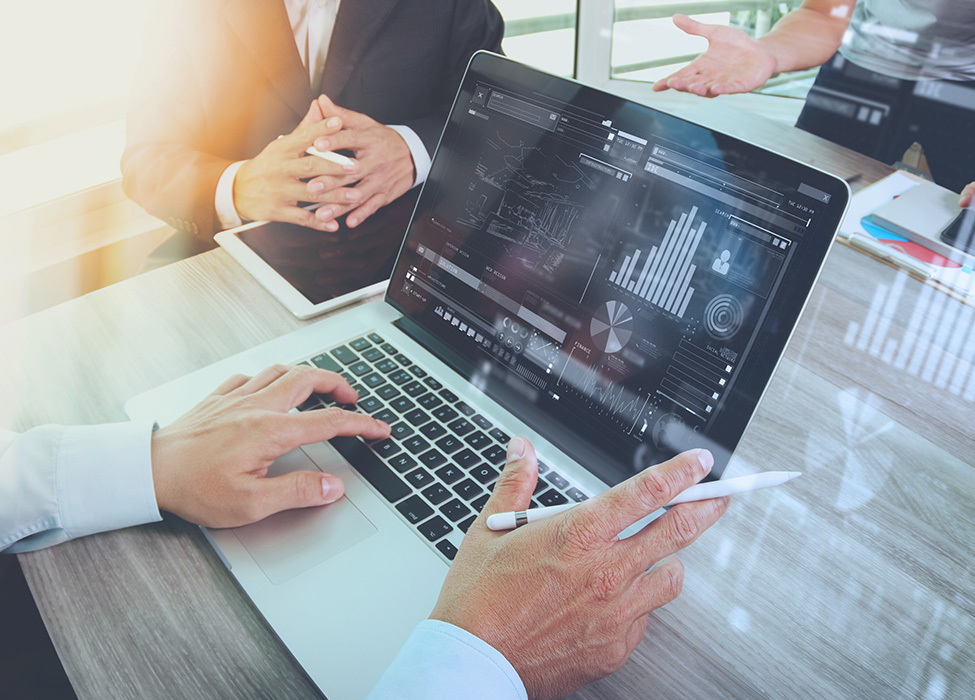 Three people sitting at the table with one person looking at a laptop with metrics