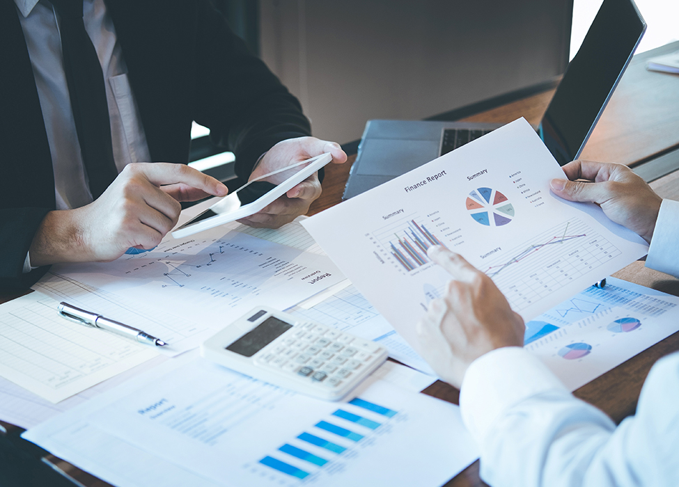 Financial Management Software | Image of two people at work sitting around at a desk with financial reports and graphs as they point to various papers