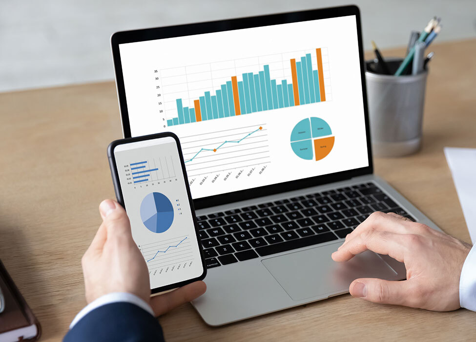 billing and payment solutions | Person looks at laptop and phone screen which displays colorful graphs